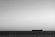 IMO condemns tanker attack near Strait of Hormuz Silhouette of cargo ship on the horizon viewed from bay with rock
