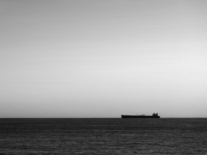 Silhouette of cargo ship on the horizon viewed from bay with rock
