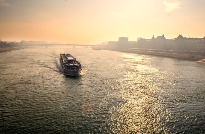 An elegant ferry navigates a tranquil river against a stunning sunset backdrop, showcasing urban beauty.
