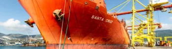 The container ship Santa Cruz berthed alongside yellow quay cranes at a container terminal.