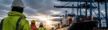 German port workers overlooking a container ship and cranes at a major seaport amid an ongoing wage dispute.