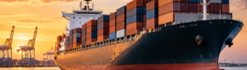 Container ship sailing near a busy port at sunset, illustrating the proposed ZIM and Hapag-Lloyd transaction.